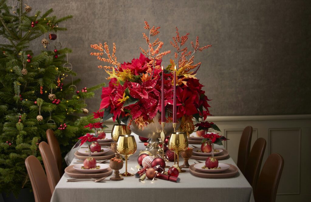 a table with white table cloth and silver vase filled with red flowers